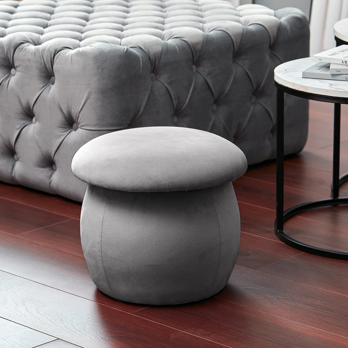 Gray ottoman in a living room setting with a tufted gray sofa and marble table.