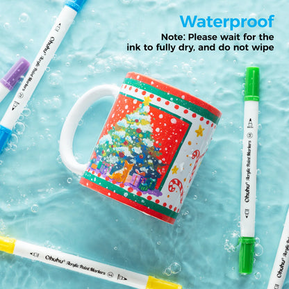 Colorful mug with Christmas design surrounded by acrylic paint markers on a water surface.