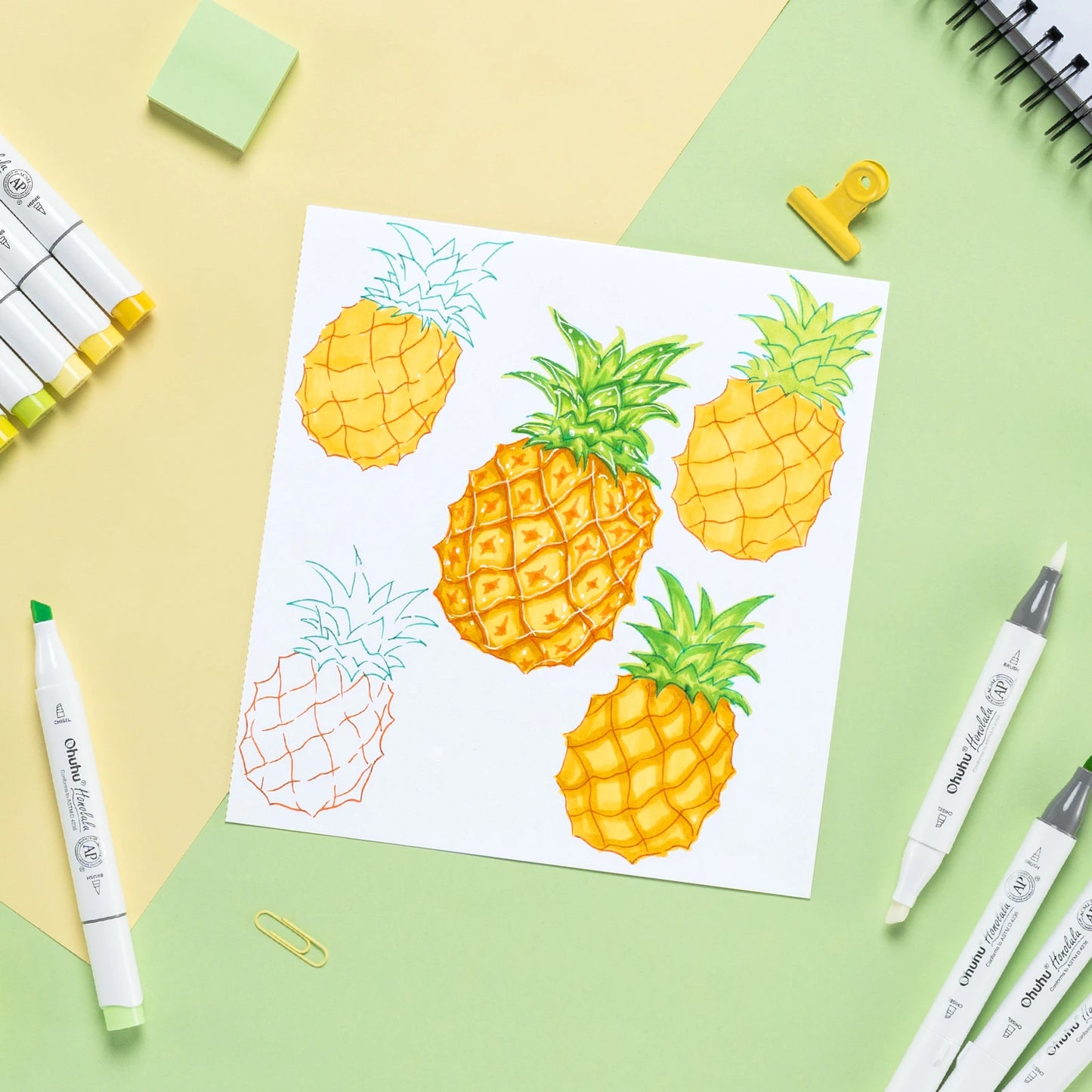 Coloring book with pineapple designs on a colorful background with markers and paper clips.