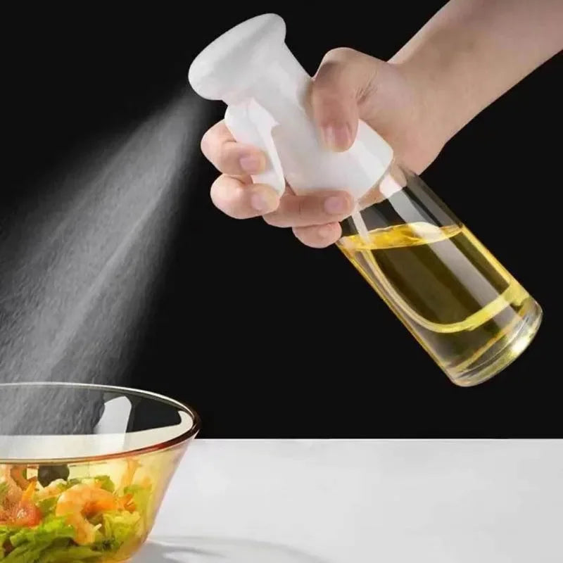 Hand holding a white spray nozzle over a glass bottle of oil with a salad in the foreground.