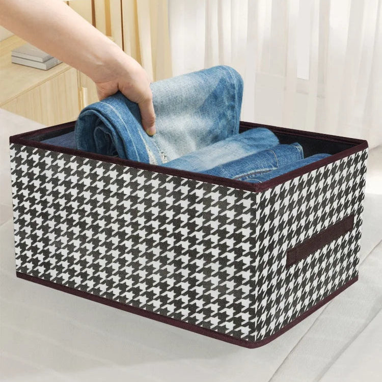 Black and white checkered storage box with jeans being placed inside, on a light-colored surface.