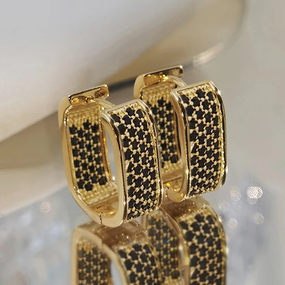 Gold hoop earrings with black gemstones on a reflective surface