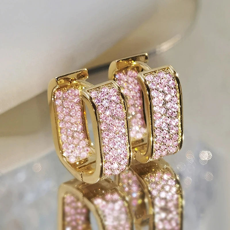 Gold hoop earrings with pink gemstones on a reflective surface