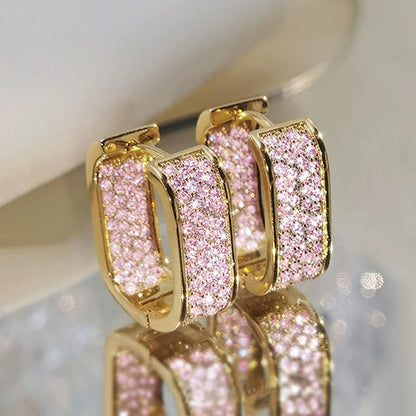Gold hoop earrings with pink gemstones on a reflective surface