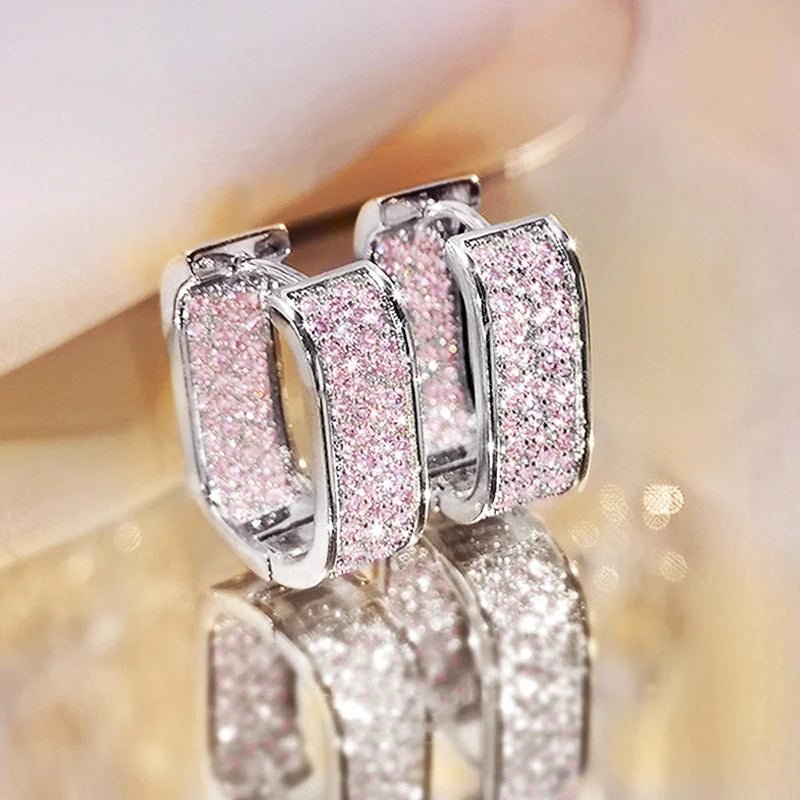 Pair of glittery hoop earrings on a reflective surface with a blurred background
