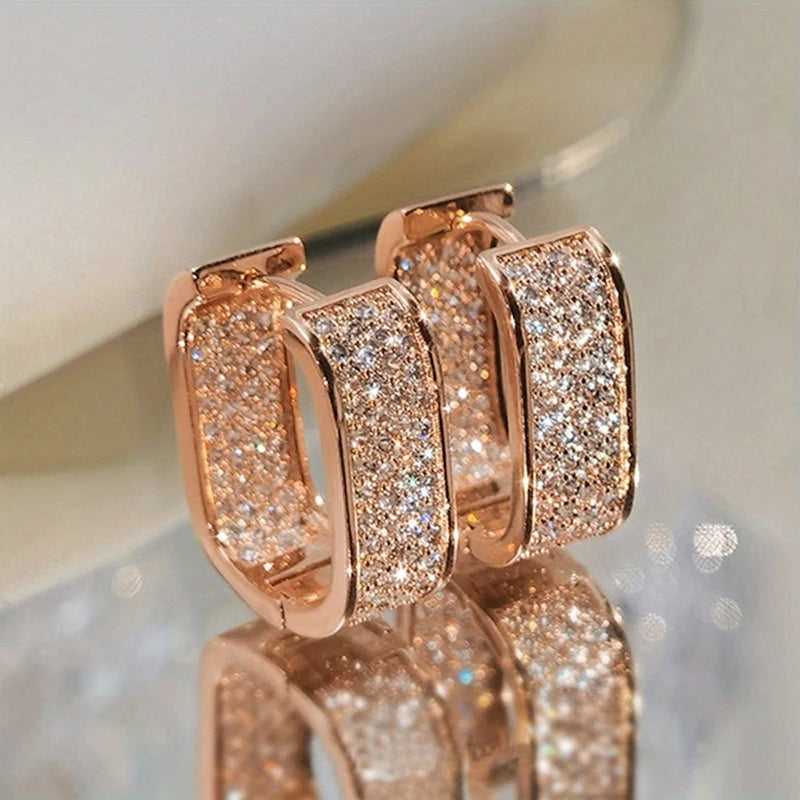 Rose gold hoop earrings with sparkling stones on a reflective surface.