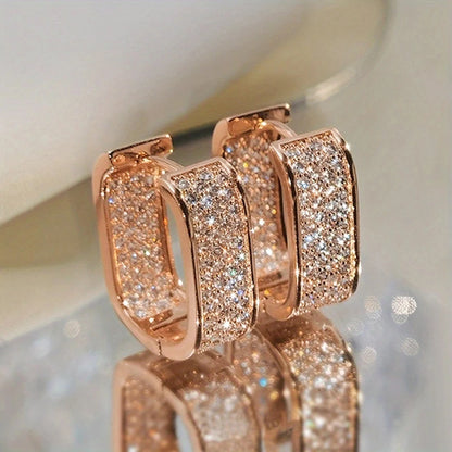 Rose gold hoop earrings with sparkling stones on a reflective surface.