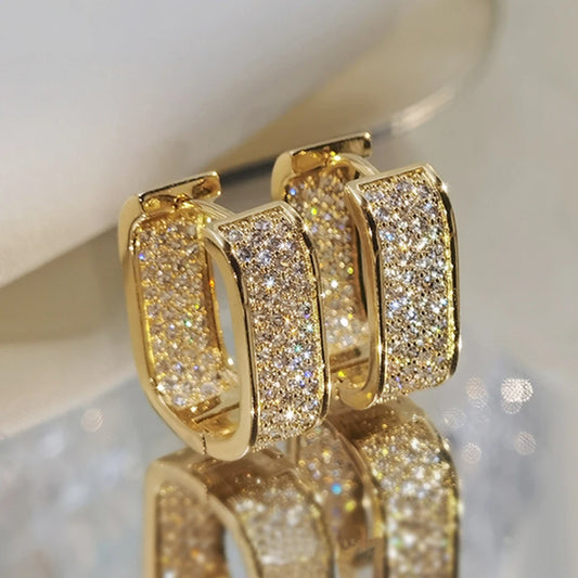 Gold hoop earrings with diamond accents on a reflective surface