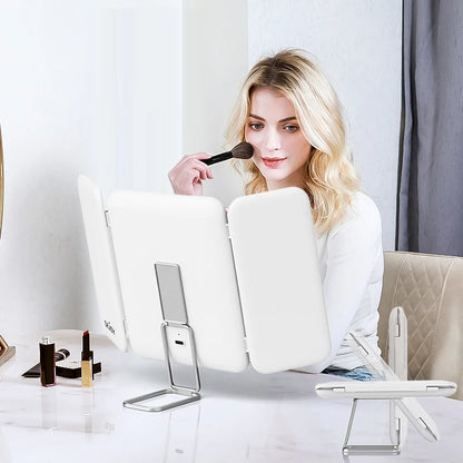 Woman applying makeup with a brush in front of a white mirror on a table.