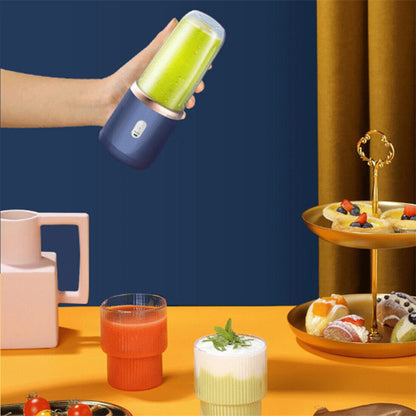 Hand holding a portable blender with a green smoothie, surrounded by food items on a table.