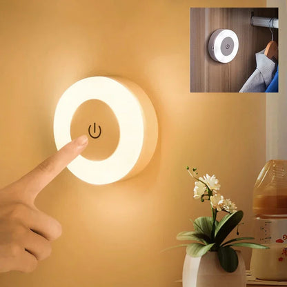 Round wall light with power symbol, hand pressing it, plant, and coffee maker in the background.