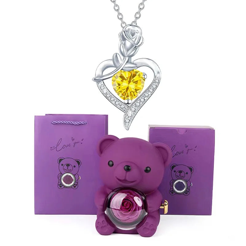 Purple teddy bear with rose and heart-shaped necklace with yellow gem on white background
