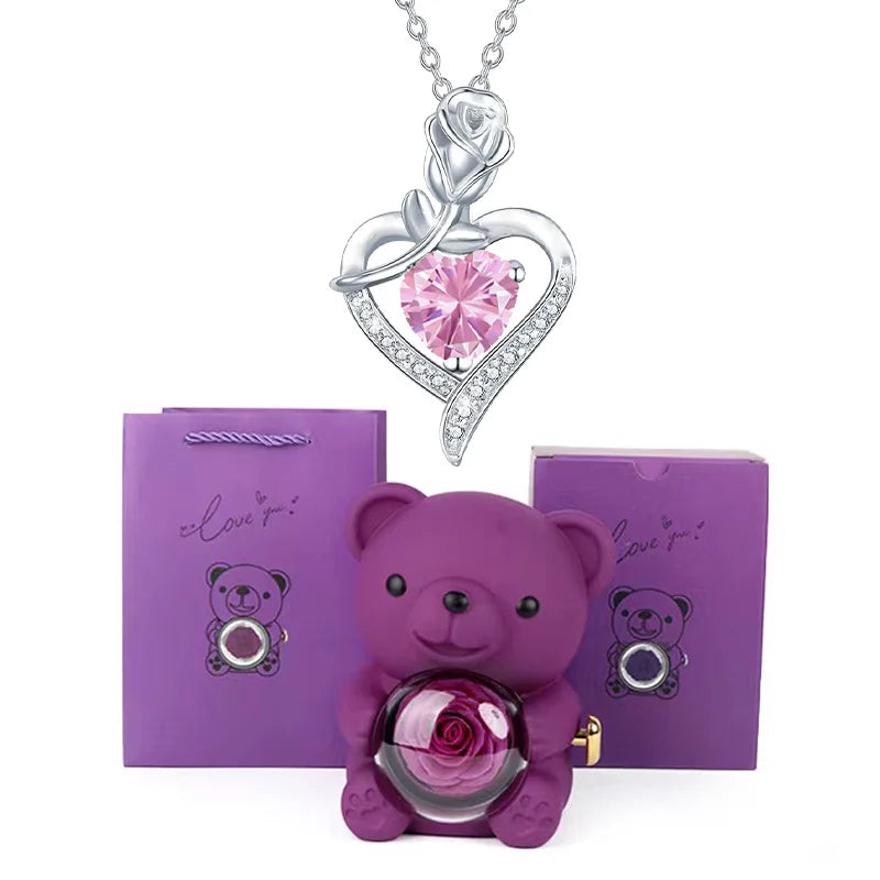 Purple teddy bear with rose and heart-shaped pink gem necklace on white background