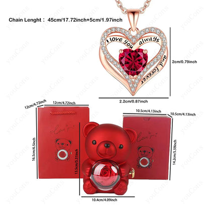 Heart-shaped necklace with red gem and dimensions, red teddy bear-shaped perfume bottle with rose, and red box with measurements on a white background.