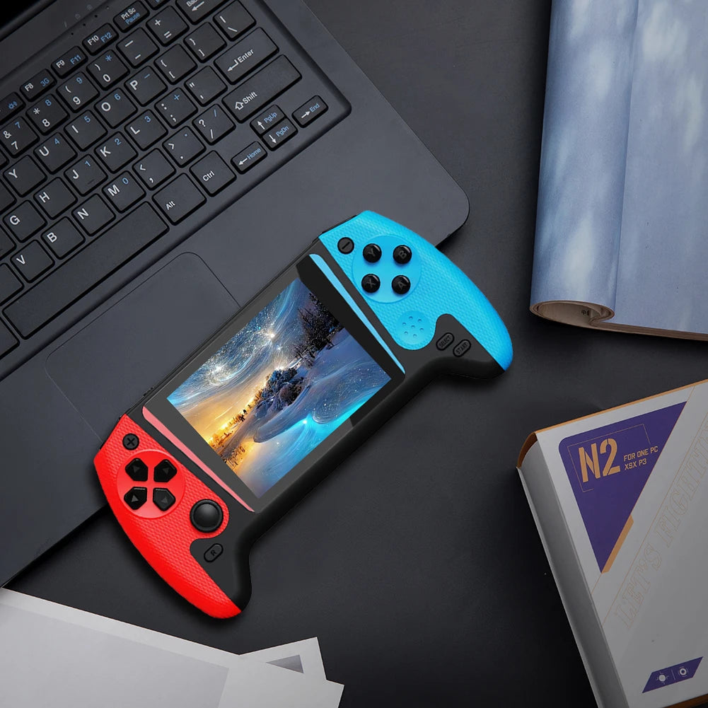 Red and blue gaming controller with screen on a dark surface next to a laptop.