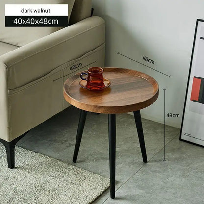 Small round wooden table with black legs next to a beige sofa, showing dimensions.