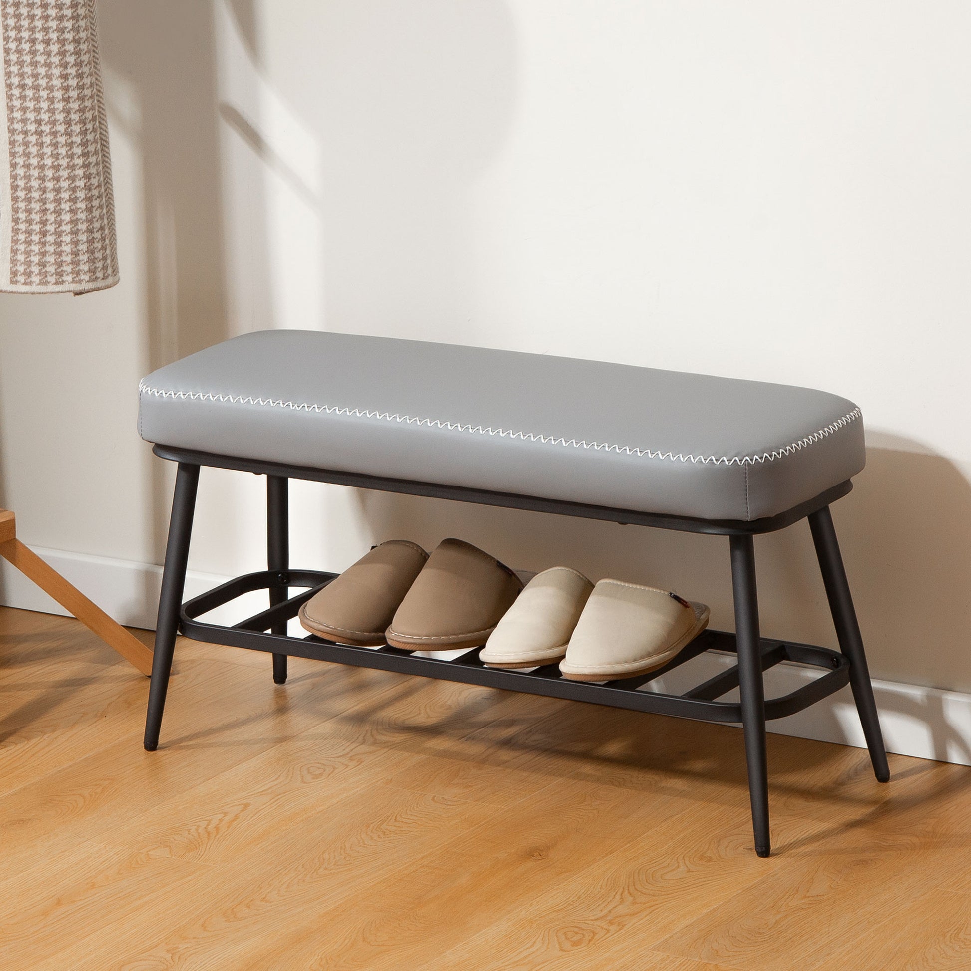 Gray upholstered bench with shoe storage shelf on a wooden floor.