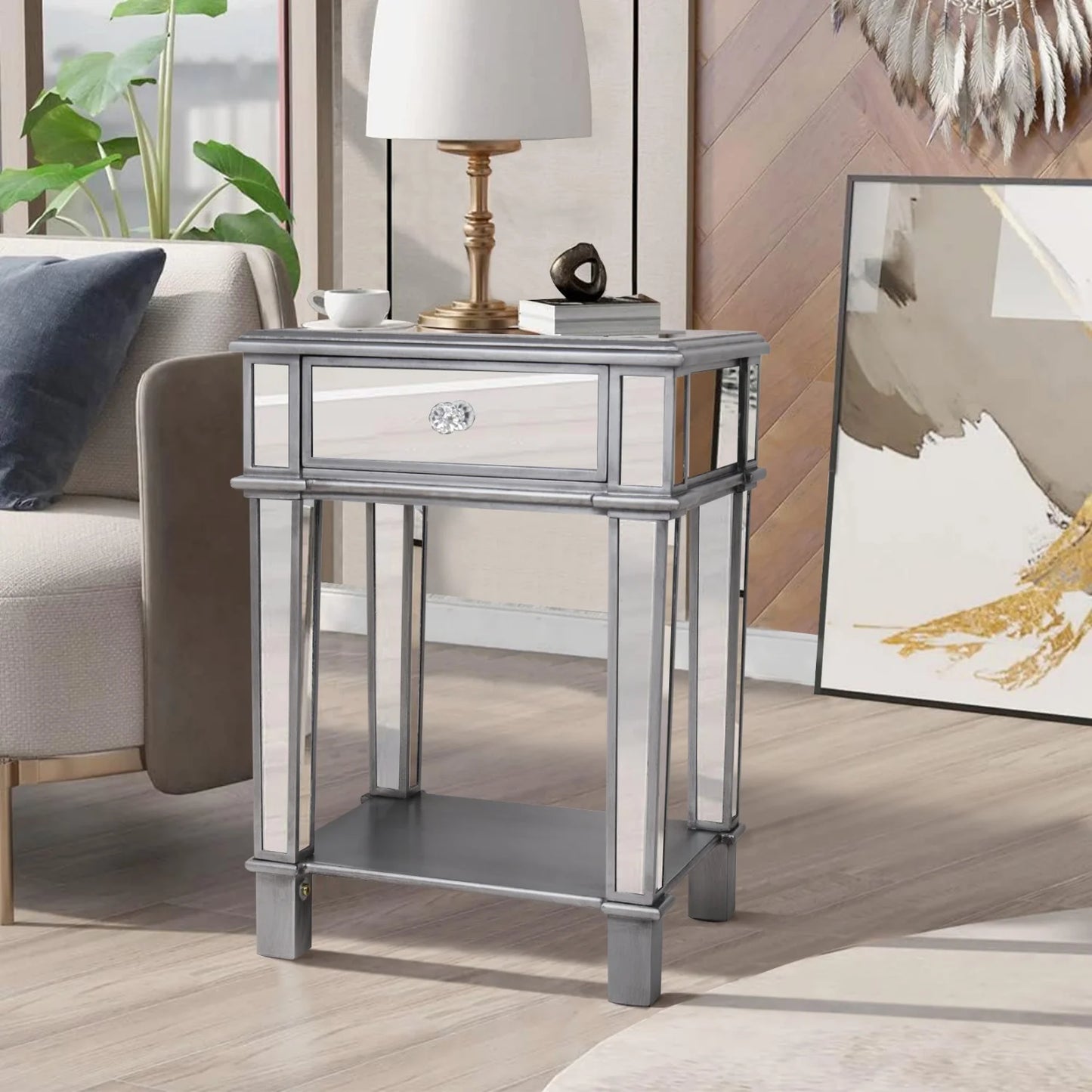 Silver mirrored side table with a lamp and decor items in a living room setting.