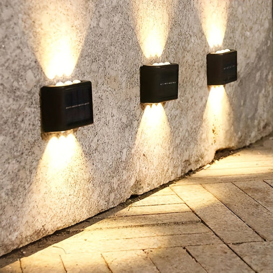 Three outdoor wall lights mounted on a stone wall casting light onto a paved ground.