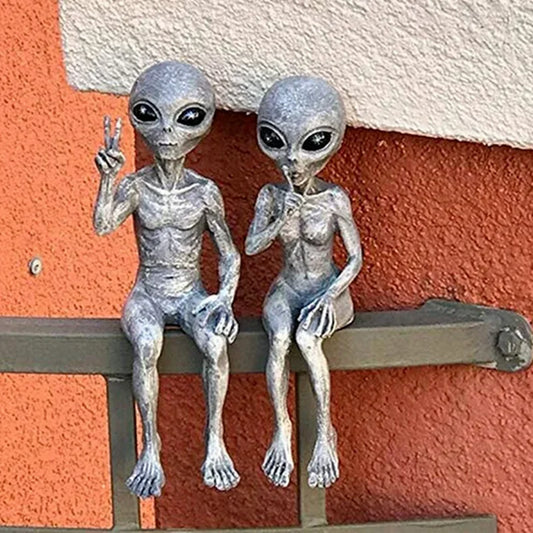 Two alien figurines sitting on a ledge with a colorful wall background