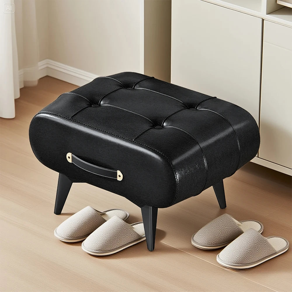 Black tufted ottoman with gray slippers on a wooden floor.