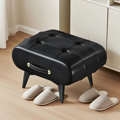 Black tufted ottoman with gray slippers on a wooden floor.