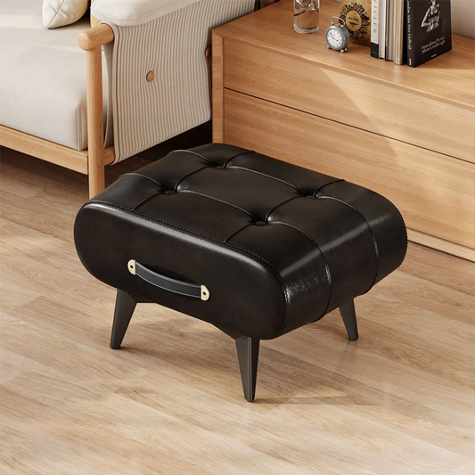 Black leather ottoman on a wooden floor with a bed and nightstand in the background.