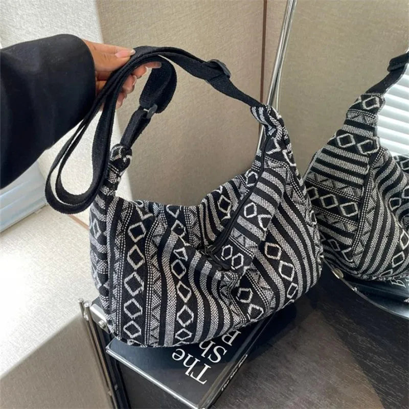 Black and white patterned handbag held by a person with a laptop underneath.