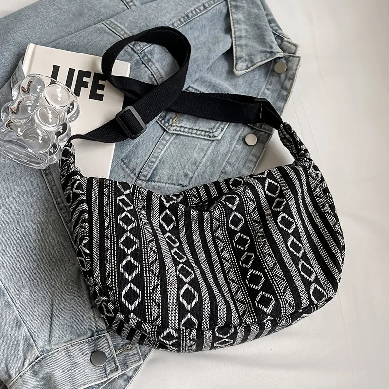 Black and white patterned bag on a denim jacket with a glass of water and a magazine.
