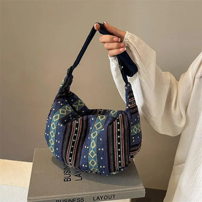 Person holding a blue patterned handbag on a beige surface