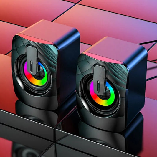 Two black cube-shaped speakers with colorful LED lights on a reflective surface.