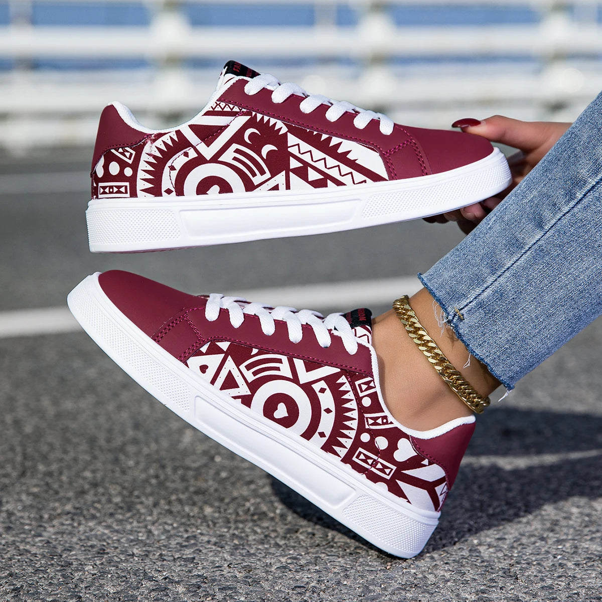 Maroon sneakers with white tribal patterns worn by a person on a blurred street background