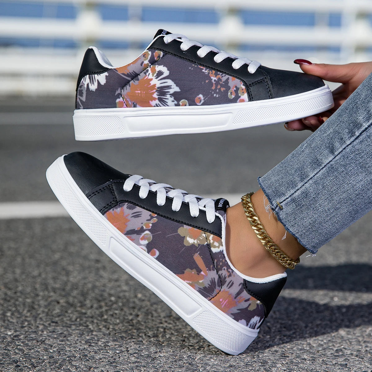 Black floral sneakers with white soles worn by a person on a road.