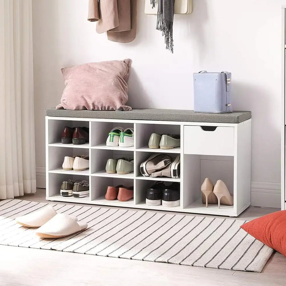 White shoe storage bench with shoes in a room with a plant and pillows.