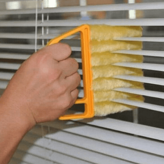 Hand using a yellow brush with an orange handle to clean blinds.