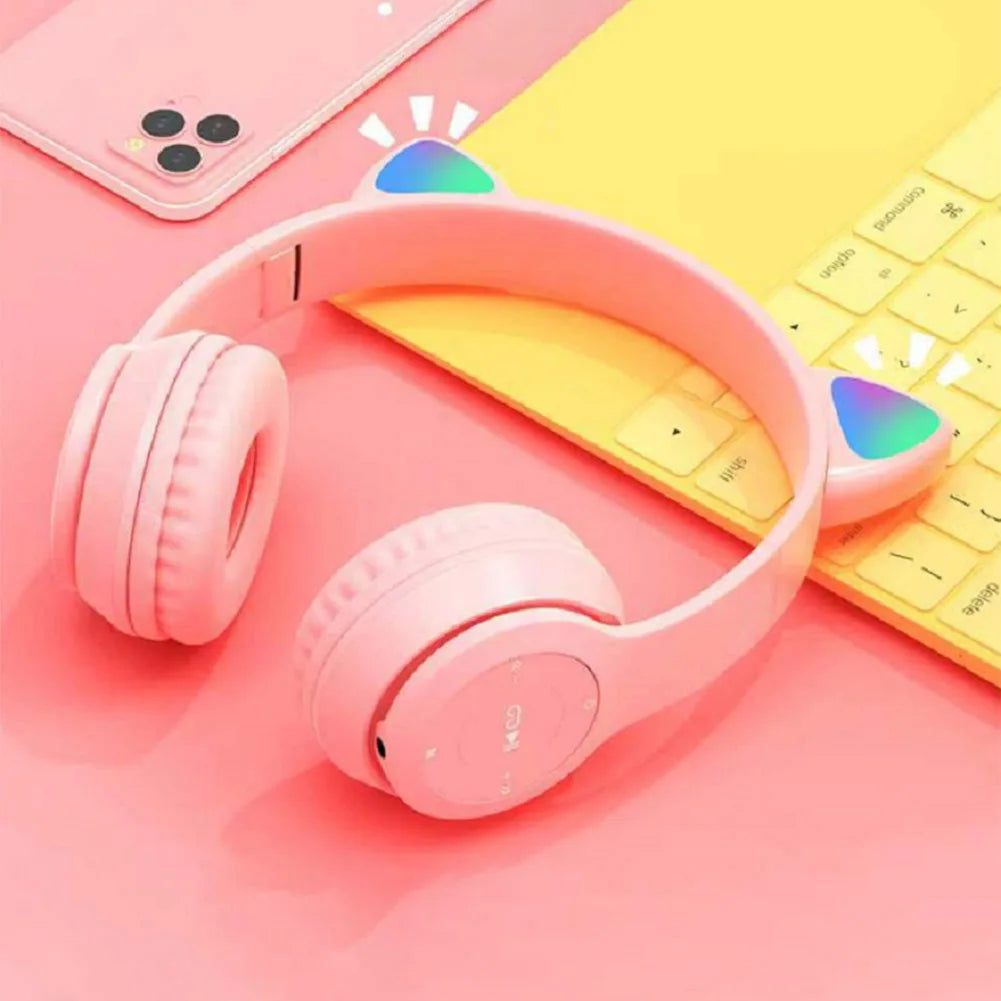 Pink headphones with colorful accents on a pink surface with a yellow keyboard and phone.