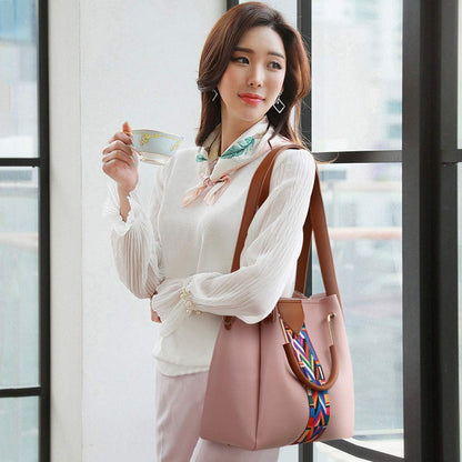 Woman holding a cup and a pink handbag with a colorful strap in front of a window.