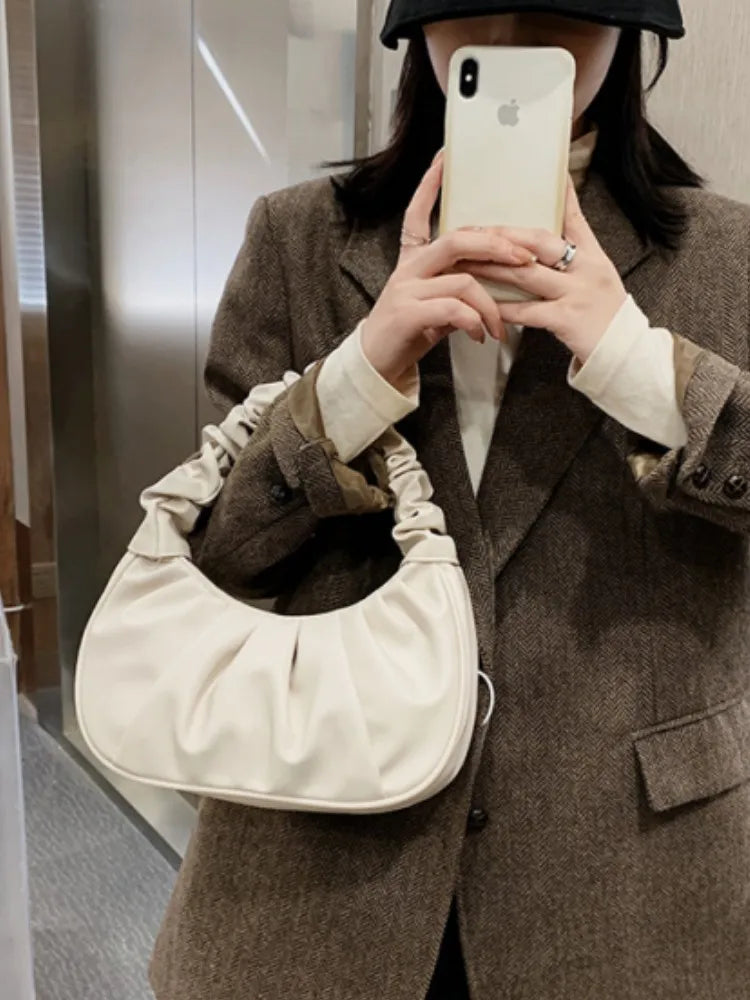 Person wearing a brown coat holding a beige handbag and taking a selfie.