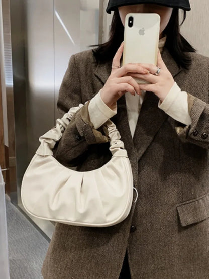 Person wearing a brown coat holding a beige handbag and taking a selfie.