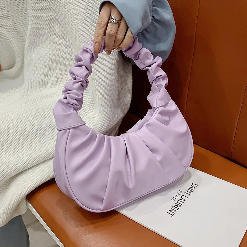 Person holding a lavender handbag on a brown surface with a brand name visible