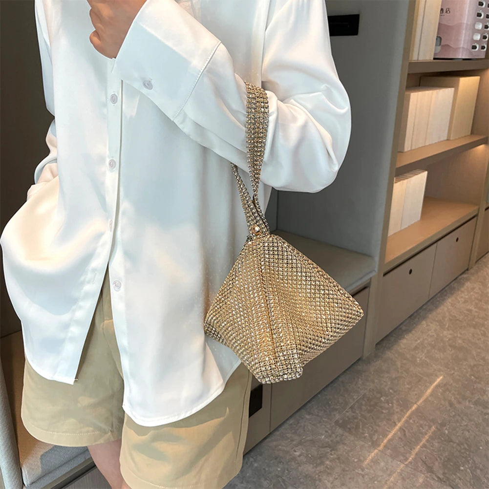 Person wearing a white shirt and beige pants holding a gold mesh handbag.