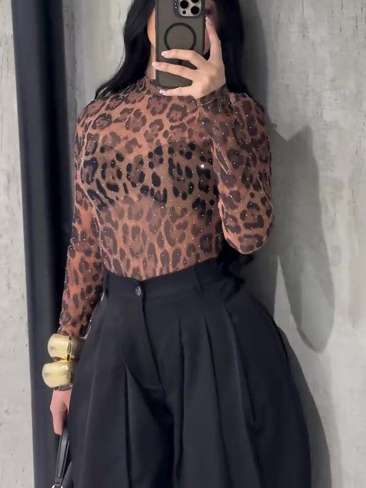 Person wearing a leopard print top and black skirt against a gray wall.