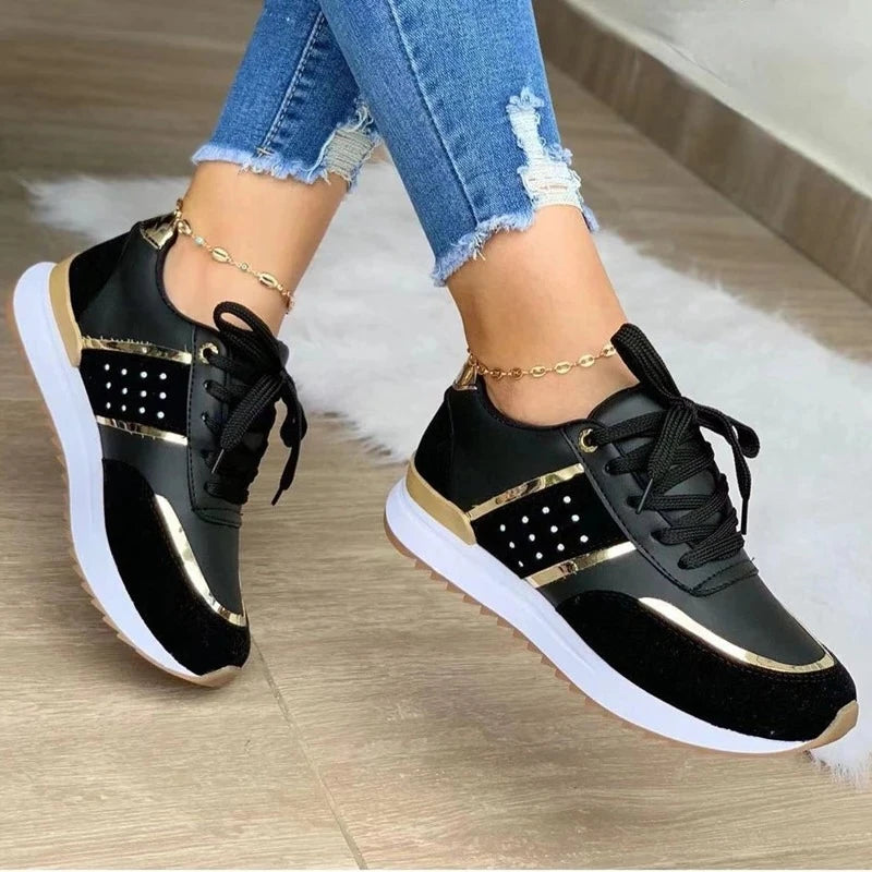 Black and gold sneakers worn with blue jeans on a wooden floor.