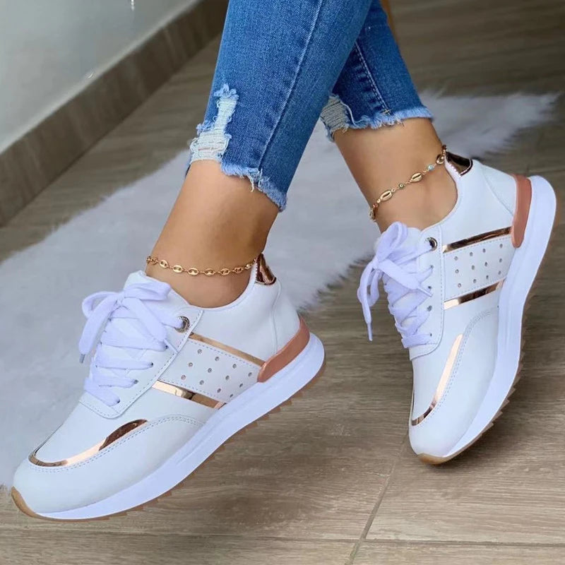 White sneakers with rose gold accents worn with blue jeans on a wooden floor.