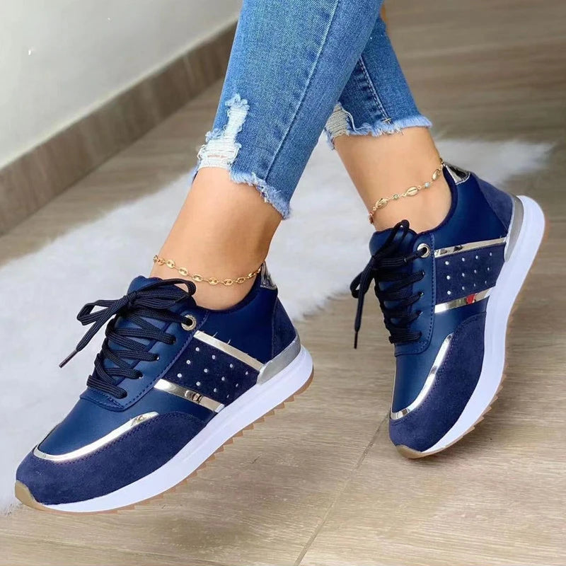 Navy blue sneakers with white soles worn by a person on a wooden floor.