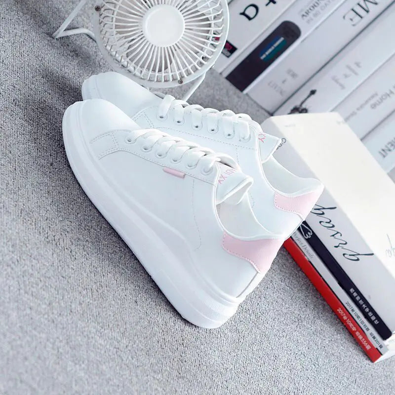 White sneakers with pink accents on a textured surface with a small fan and books.